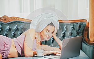 Distance online working from bed. Young attractive woman with coffee and laptop relaxing at home. Cozy lazy mornig