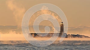 In the distance the outline of a lighthouse disappears and reappears as the sea smoke shifts with the wind photo