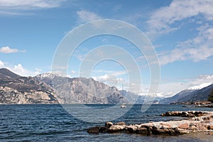 In the distance, a sailing yacht sails along the sea bay against the background of mountains and a blue sky. Picturesque seascape