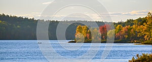 In the distance, two people in a boat. Late summer afternoon, sun shines golden light on a lake.