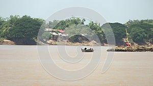 Distance view of a small motorized dugout canoe pulling behind a large heap of bamboo poles down the river 