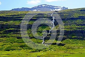 The distance view of the tall waterfalls near Seydisfjordur, Iceland during the summer