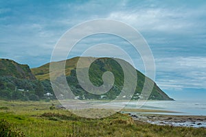 Distand couple walking along vast ocean beach surrounded by rugged mountains. Heavy clouds and thick mist over riptide photo