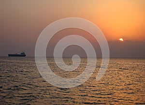Distant crude oil taker on a sunset time against the sun in calm sea waters
