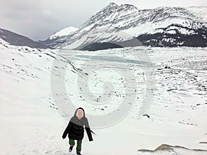 A distant faraway view of a female hiker alone walking through the vast winter landscape towards the athabasca glacier