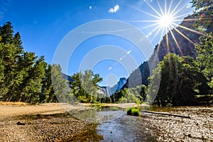 A distant half dome in the center and a sunburst on the right looking down the Merced River in Yosemite National Park