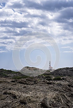 distant image of the Favaritx lighthouse, with a rock formation around it on a cloudy summer day, vertical, copy space