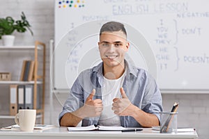 Distant learning language. Smiling young male teacher showing thumbs up and explaining english rules to students