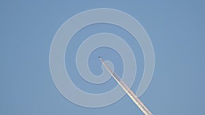 Distant passenger jet plane flying on high altitude on clear blue sky leaving white smoke trace of contrail behind. Air