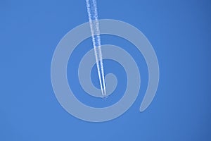 Distant passenger jet plane flying on high altitude on clear blue sky leaving white smoke trace of contrail behind. Air