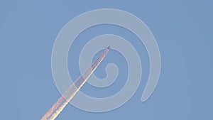 Distant passenger jet plane flying on high altitude on clear blue sky leaving white smoke trace of contrail behind. Air