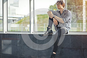 Distant plan of young man sitting next to big windows at metro station.