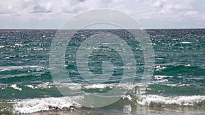 Distant Sailboat With Ocean Waves And Cloudy Sky From Shore