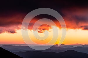 Distant sunset above layers of mountains and valleys with mist and fog, with a rooftop of close red clouds