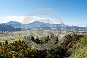 Distant view of Aso valley and mountain ridge with Mount Aso volcano venting steam on sunny autumn day, Japan.