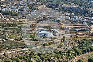 A distant view of cultivated land and green fields under a bright blue sky with mountains in the background