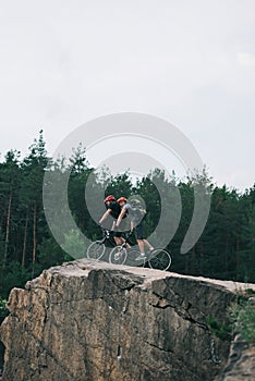 distant view of male extreme cyclists in protective helmets riding on mountain bicycles on rocky cliff