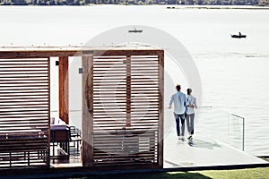 distant view of stylish couple standing on pier near lake at country