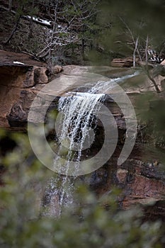 Distant View of Water Falling Over Red Sandstone Cliffs with Branches in Winter