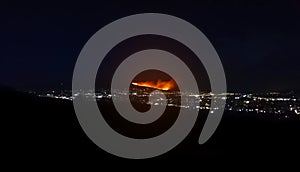 Distant wild fire on a mountain above the city at night. Dark scenery with urban lights.