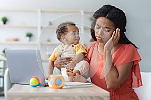 Distant Work During Maternity Leave. Stressed Black Woman With Baby Using Laptop