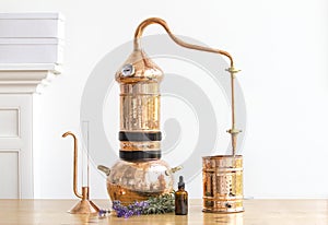 Distilling apparatus alembic with esential oil flowers at the wooden table