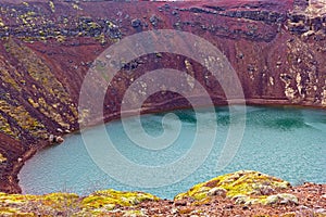 Distinctive red rock and vegetation on one edge of a volcanic crater lake in south Iceland.