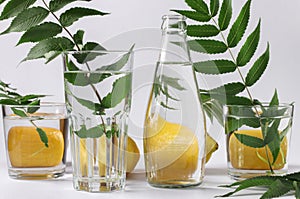 Distorted lemons and green leaves lie behind glass vessels on white background. Distortion of an object through