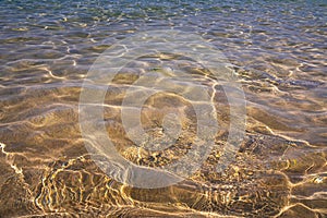 Distorted texture of sand under water. Transparent water ripples, sand waves and glare of sunlight. Seabed background