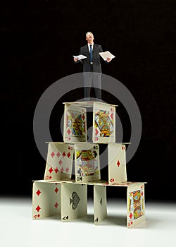 Distraught man in business suit standing on house of cards