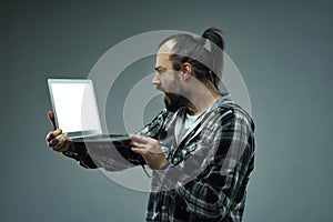 Distraught man staring at his handheld laptop screen in horror