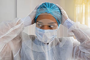 Distraught nurse wearing protective workwear while holding her head in pain at medical clinic