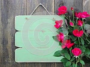 Distressed blank green sign with flower border of red roses hanging on rustic wood door