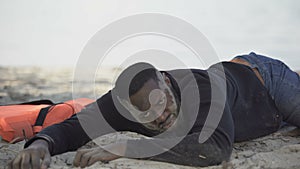Distressed refugee lying on beach, looking with plea asking help, crash survivor