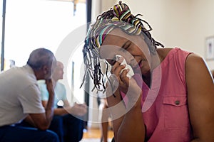 Distressed senior biracial woman holding tissue and crying in group therapy session