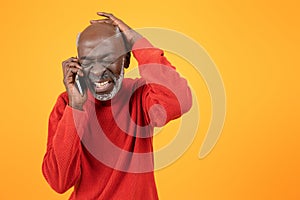 Distressed senior Black man in a red sweater, talking on a smartphone with a painful expression