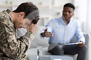 Distressed young man soldier attending therapy session with psychiatrist