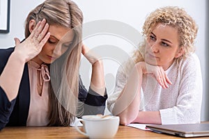 A distressed young woman in business attire is comforted by a concerned colleague, embodying the emotional toll of