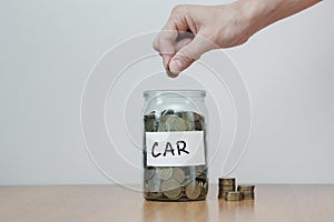 Distribution of cash savings concept. Hand puts coins to the glass money boxes with inscription `car`.