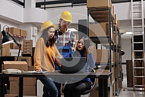 Distribution center workers checking goods supply schedule on laptop