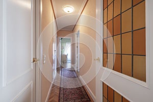 Distributor corridor of an urban residential house with white woodwork with leaded windows and parquet floors with narrow rugs