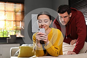 Distrustful man peering into girlfriend`s smartphone. Jealousy in relationship