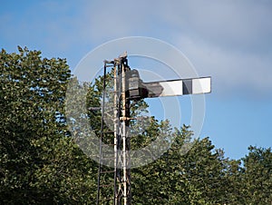 Disused train signal with a blue sky and trees