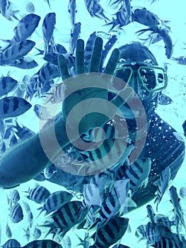 Diver man under water in a snorkeling mask shows open hand.