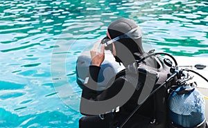 A diver in a wetsuit and mask with a scuba is about to dive into the water from a boat. Diving lessons. Close-up. Copy space