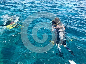 Divers in black diving waterproof suits with shiny metal aluminum canisters float, dive into blue clear sea water on vacation, sea