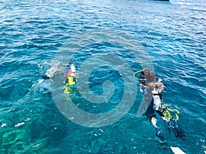 Divers in black diving waterproof suits with shiny metal aluminum canisters float, dive into the blue sea water on vacation, a sea