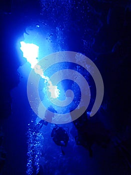 Divers Swim Through Lava Cave and Arch with Bubbles in Blue