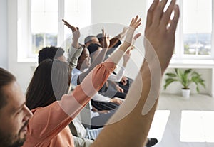 Diverse audience raising their hands to ask questions of speaker after conference