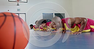 Diverse basketball players perform push-ups in a gym